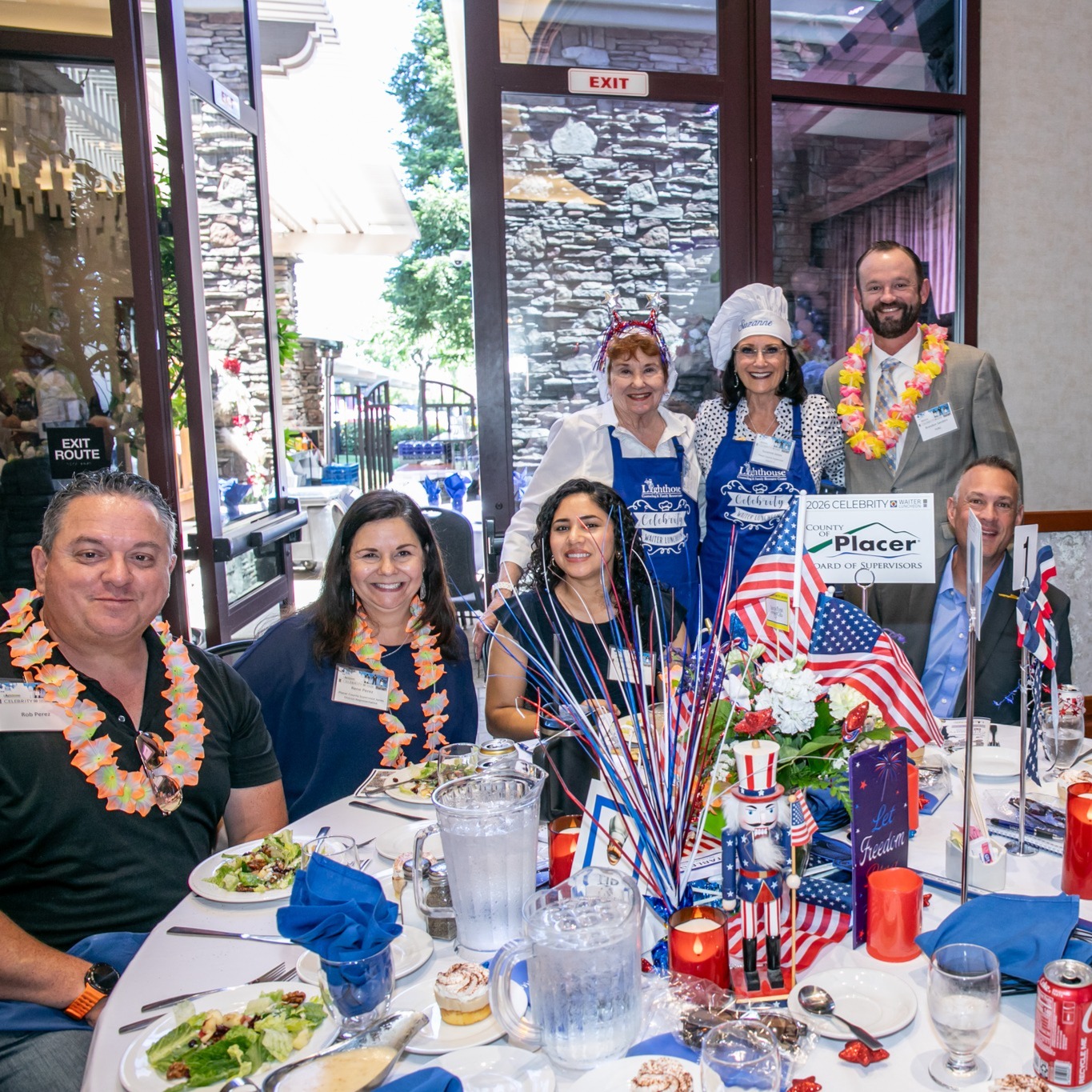 Supervisor Jones wearing a chef's hat. standing with guests at her table decorated in Red White and Blue with flags and patriotic flair
