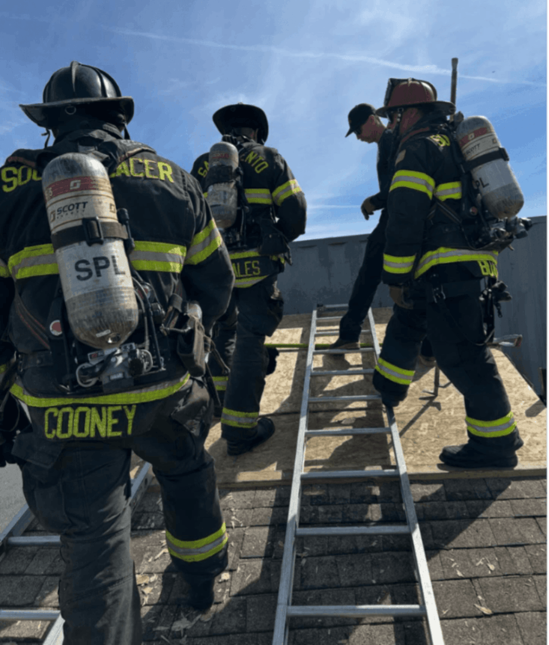 firemen climbing from a ladder to a rooftop under a blue sky