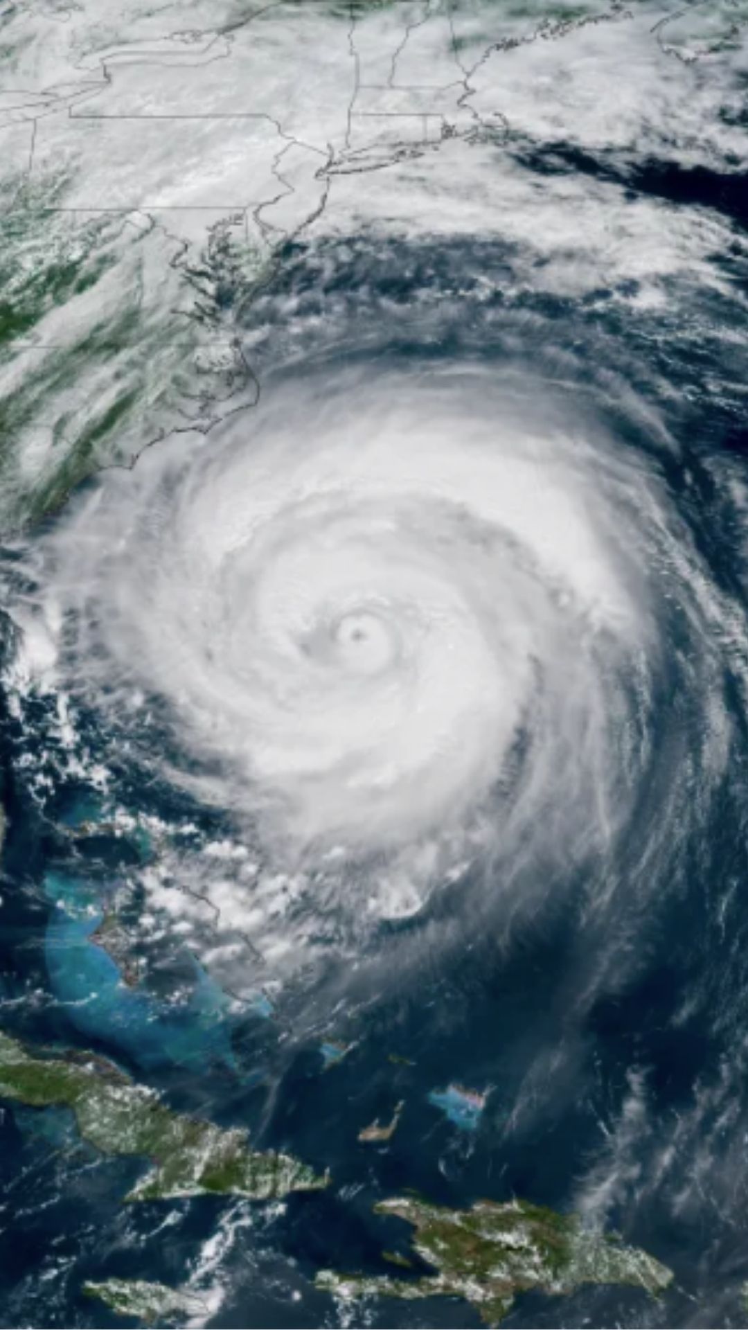 A high‑resolution satellite image showing a large, well‑defined hurricane over the Atlantic Ocean. The spiral bands of clouds extend outward from a distinct eye at the center. The storm is positioned near the southeastern coastline of the United States, with parts of Florida, Georgia, and the Carolinas visible on the left side of the image.