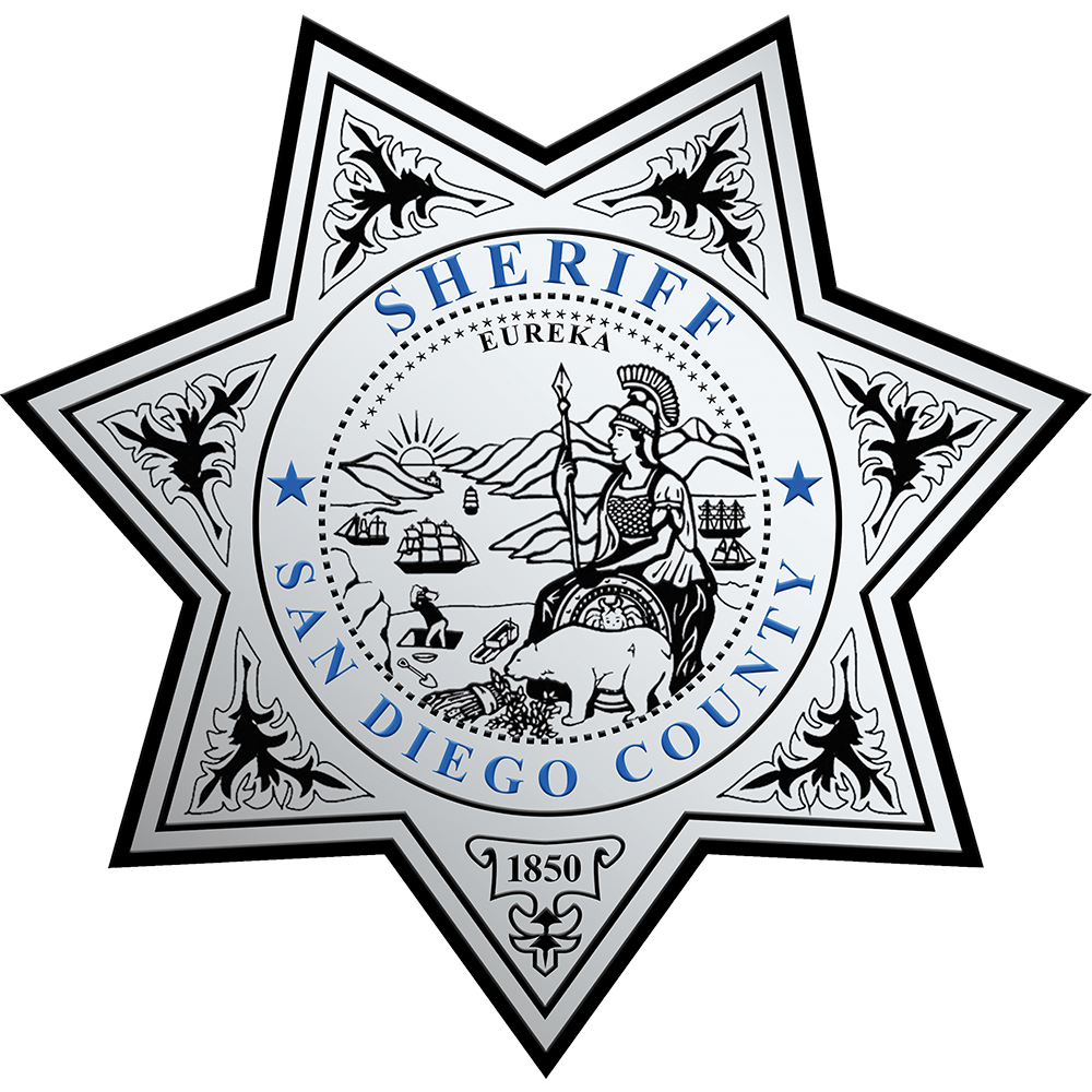 Eight‑pointed star badge featuring the official emblem of the San Diego County Sheriff’s Office. The center contains a circular seal with a seated figure holding a staff, a bear in the foreground, mountains, water, and ships in the background. Decorative leaf patterns appear on each point of the star, and the text ‘Sheriff San Diego County’ surrounds the central seal.