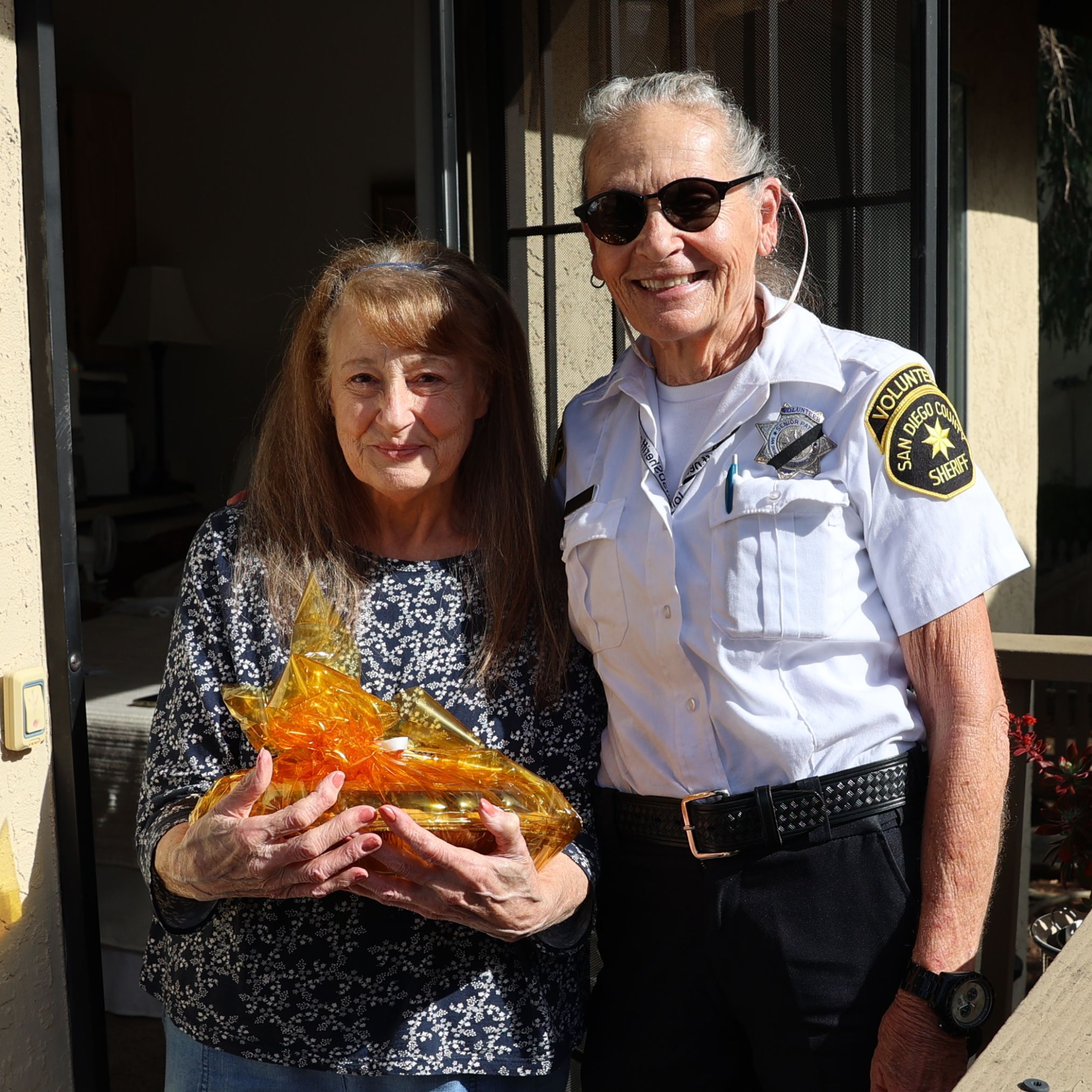 Senior Volunteer patrol giving a pie to an elderly women wearing a white shirt with a black and yellow patch.